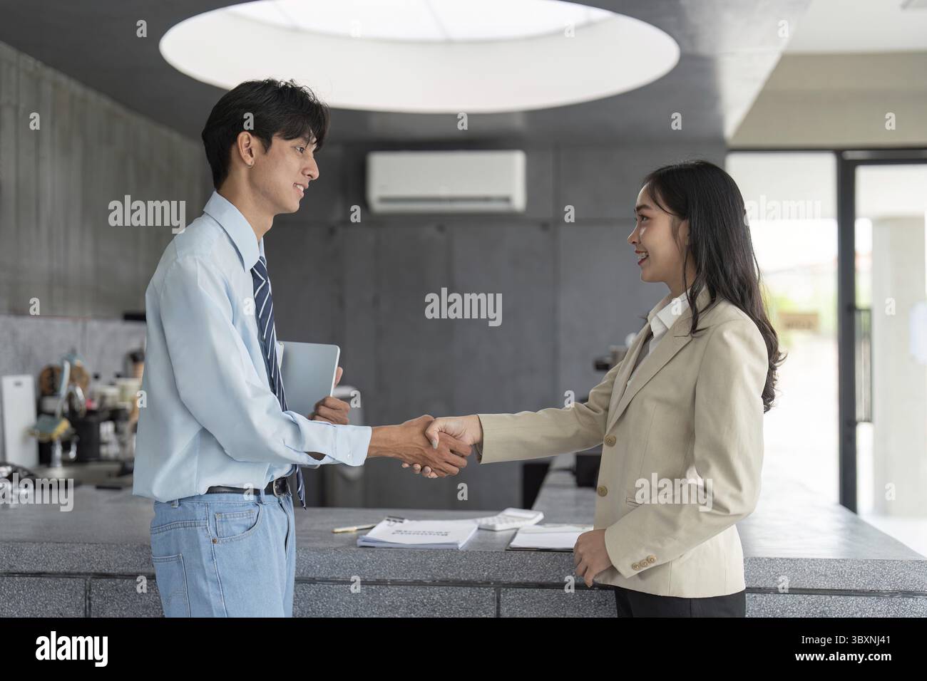 Una stretta di mano tra due professionisti in un moderno ambiente di caffetteria, che simboleggia un accordo e una partnership di successo Foto Stock