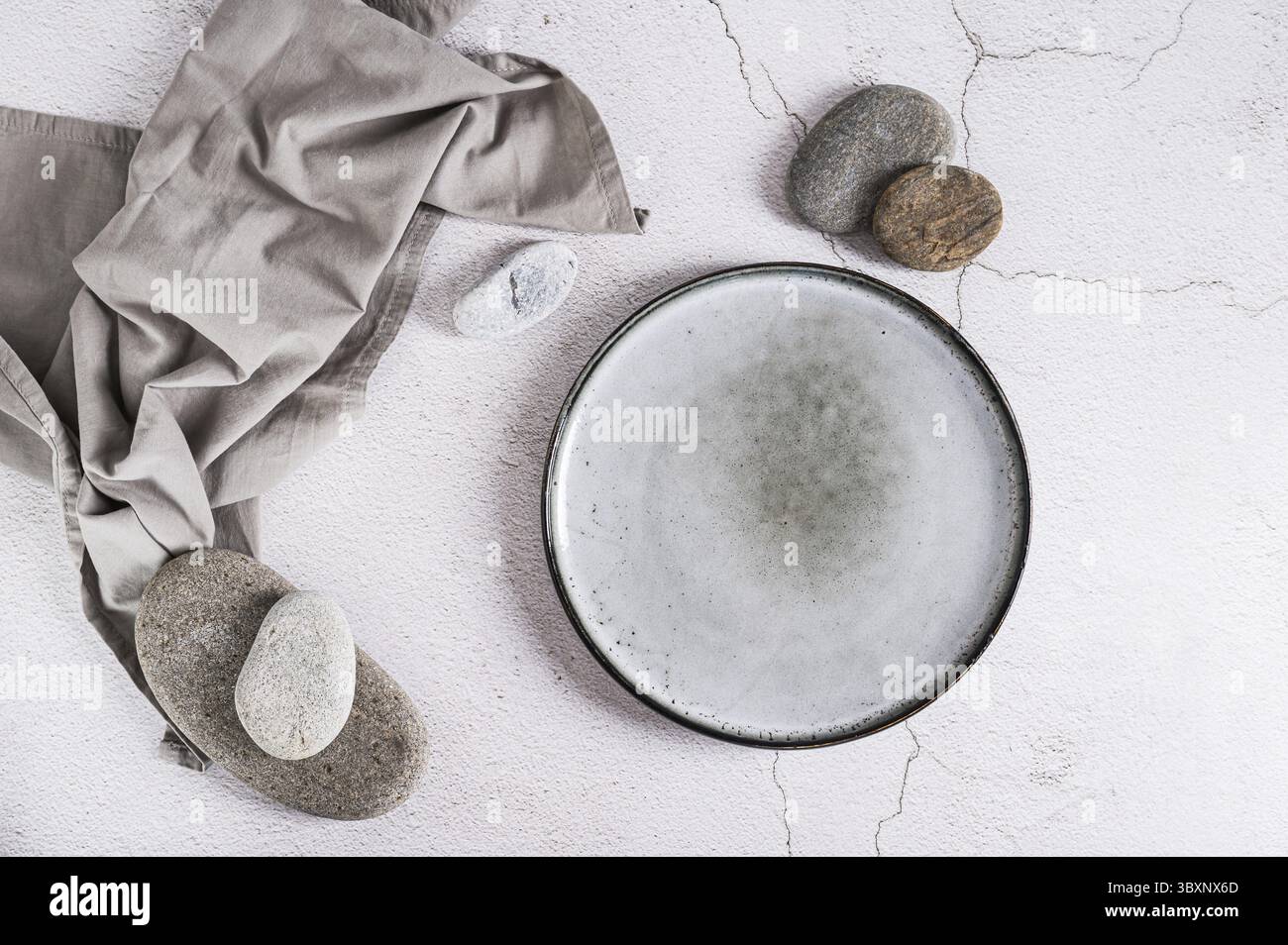 Cibo, piastra in ceramica vuota, pietre e tovagliolo su sfondo grigio vista dall'alto Foto Stock