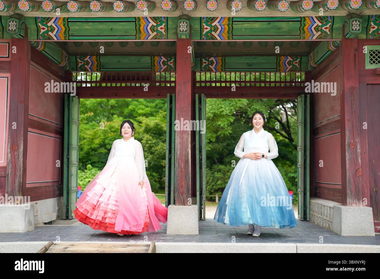 A giugno a Seul, due donne coreane sui vent'anni si stendono fianco a fianco davanti alla maestosa porta antica del Palazzo Gyeongbokgung, indossando l'affascinante spilla Foto Stock