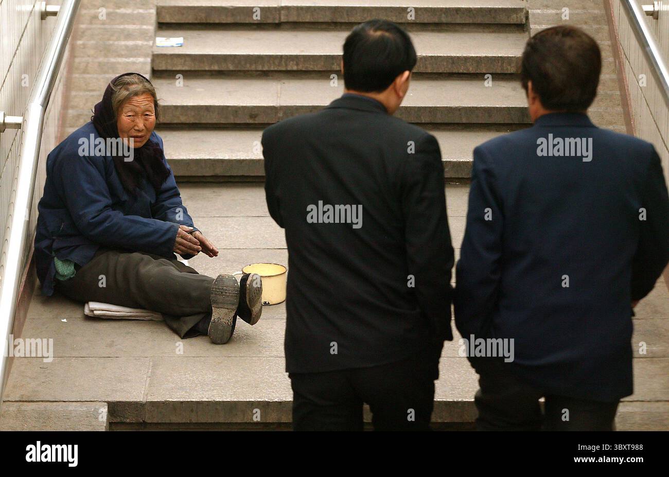 28 marzo 2006, PECHINO, CINA: Un'anziana donna chiede soldi agli uomini d'affari per le strade di Pechino, Cina, il 28 marzo 2006. Senza un sistema di previdenza nazionale o una rete di sicurezza sociale per catturare coloro che hanno un disperato bisogno di hekp medico, molti cinesi paralizzati e disabili sono costretti a difendersi e di solito finiscono per strada. Tra i cinesi che soffrono per le dure riforme economiche messe in atto alcuni anni fa, che hanno chiuso molte imprese statali, c'è la virtuale abolizione del sistema previdenziale statale che un tempo si prendeva cura di loro dalla nascita alla morte. (Credito IMA Foto Stock