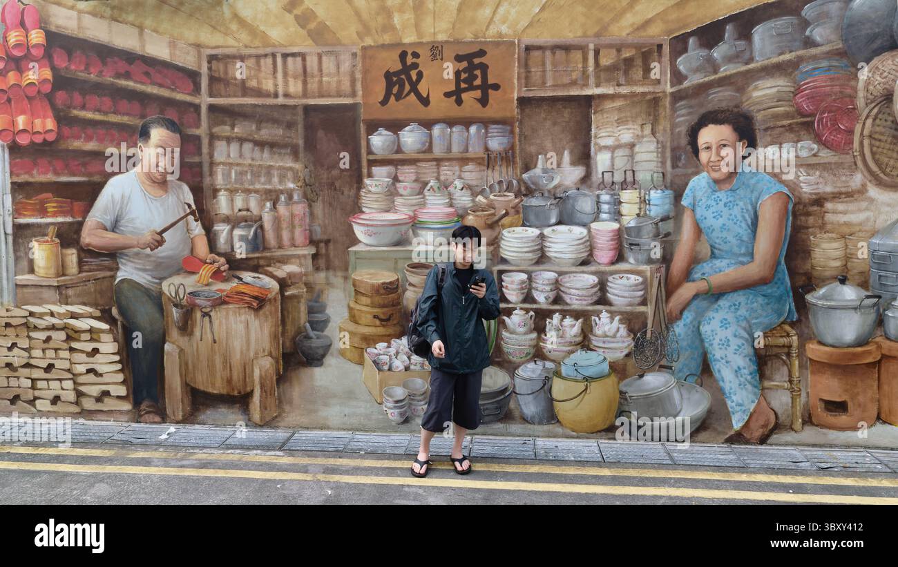 Un uomo cinese si trova di fronte a un murale a Chinatown, Singapore, raffigurante un vecchio negozio cinese di utensili per la casa e un calzolaio cinese Foto Stock