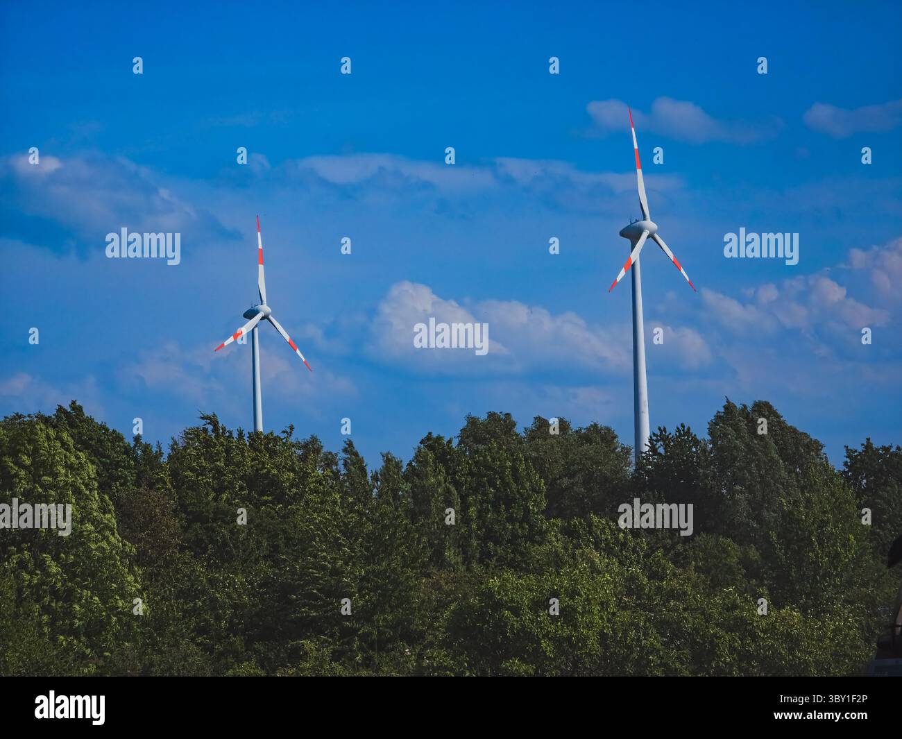 Turbine eoliche sopra la foresta verde sotto il cielo blu – energie rinnovabili, 2 giugno 2025 Foto Stock