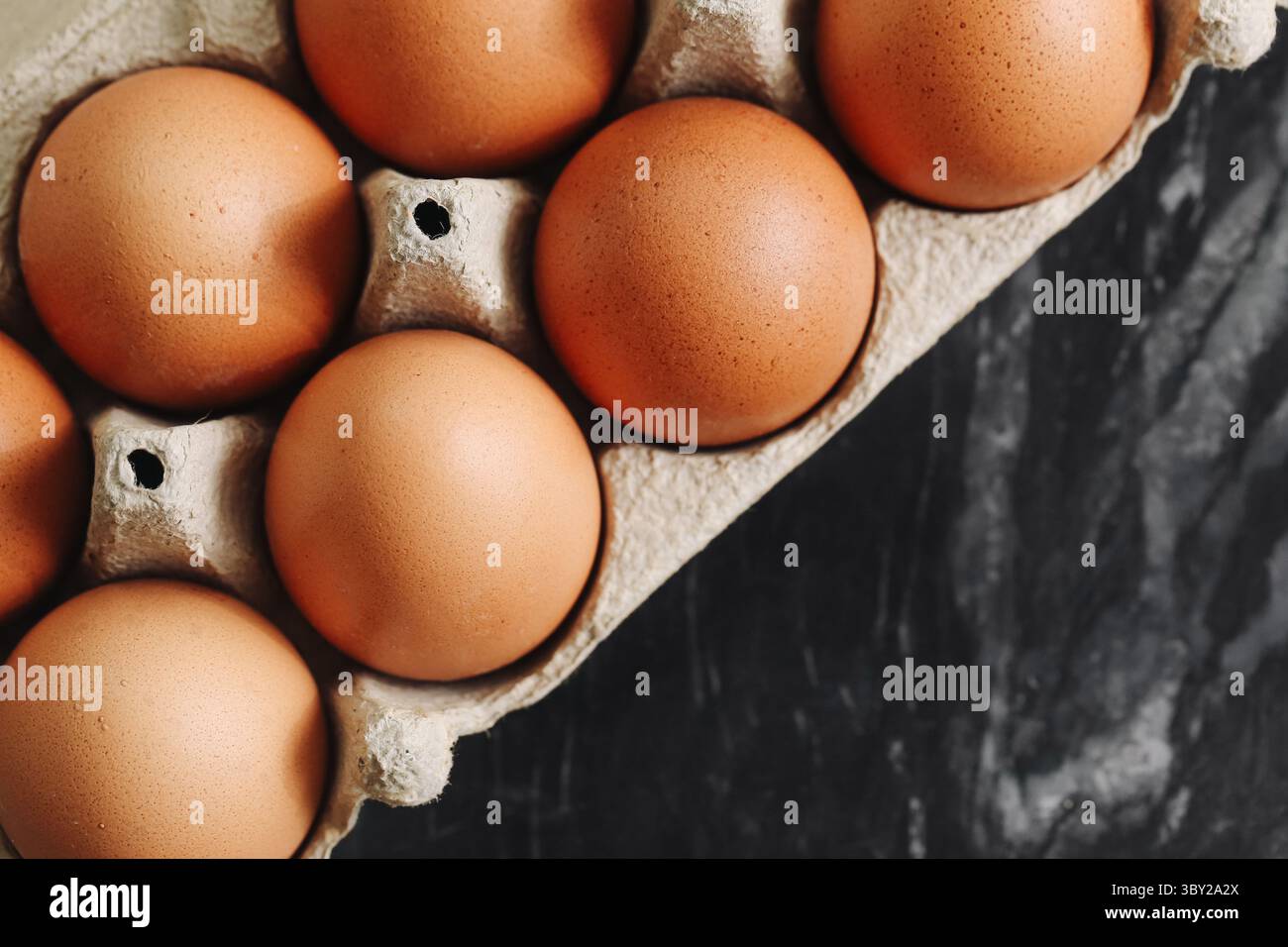 Uova di pollo marroni in cartone. Vista dall'alto delle uova fresche biologiche. Prodotto alimentare naturale. Contenitore delle uova di fattoria su pietra nera. Ingrediente salutare per la colazione. Foto Stock