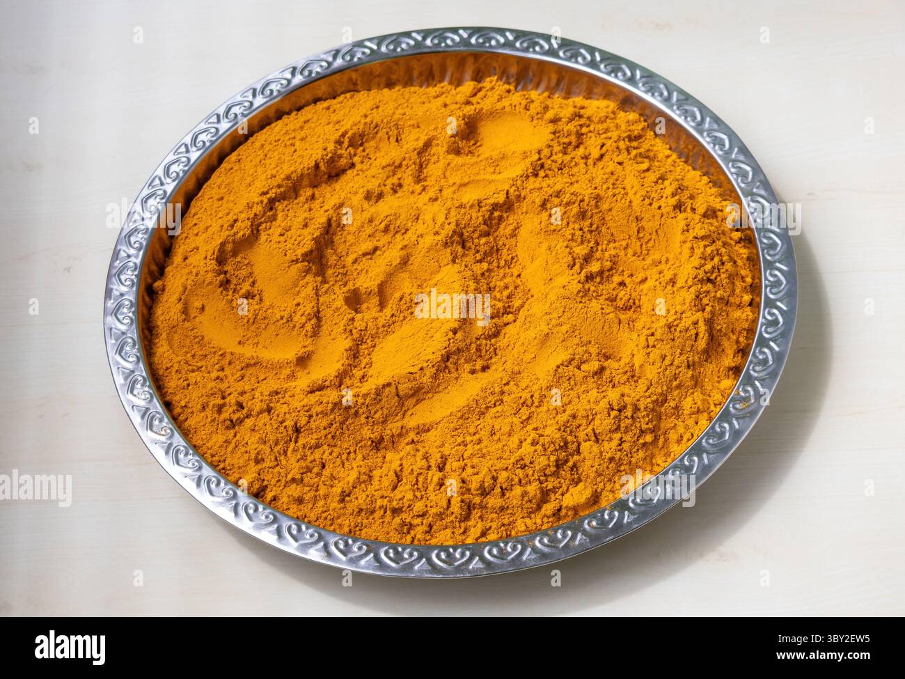 Polvere di curcuma gialla brillante in un piatto in acciaio inox dopo la frantumazione, perfetta per temi culinari e legati alle spezie. Colori naturali e vivaci, sani Foto Stock