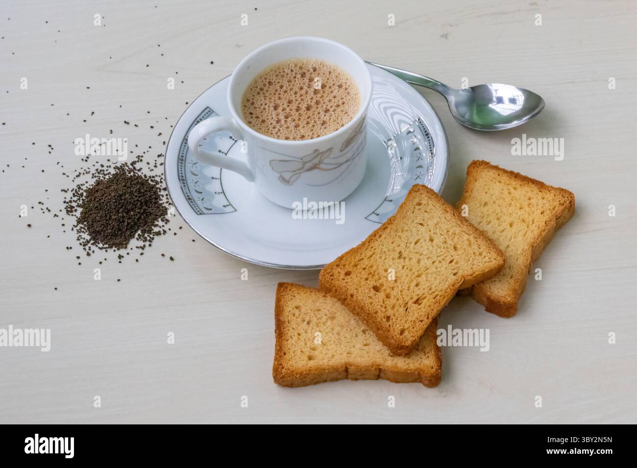 Tè al latte caldo e schiumoso in un teacup con biscotti dorati al crespo. Foglie di tè fresche e secche sparse su una superficie di legno, catturando l'essenza di un intimo Foto Stock