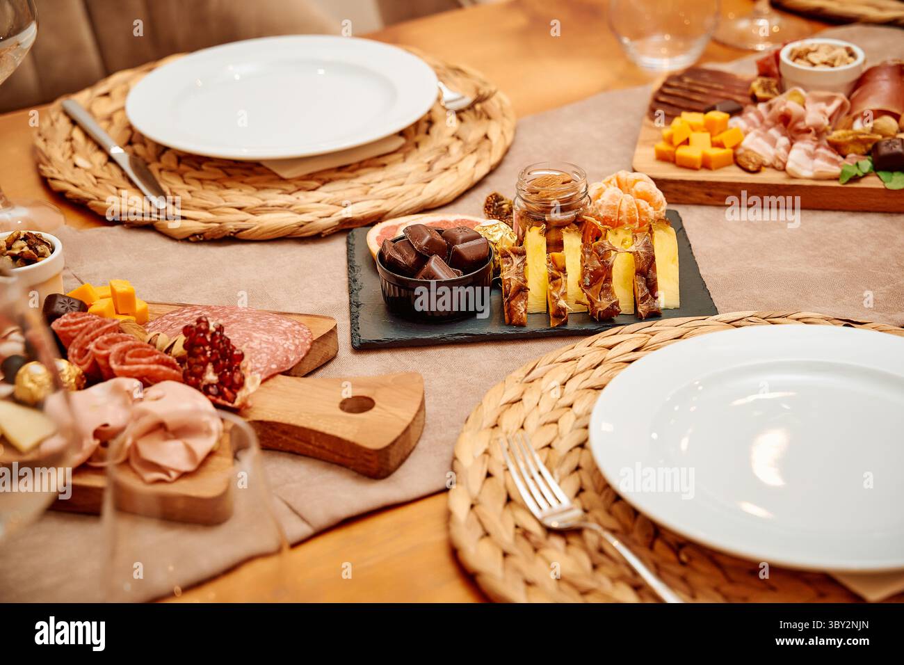 Un tavolo da pranzo elegantemente organizzato con un tagliere di salumi e un vassoio di frutta con una squisita selezione di formaggi, noci e affettati. Foto Stock