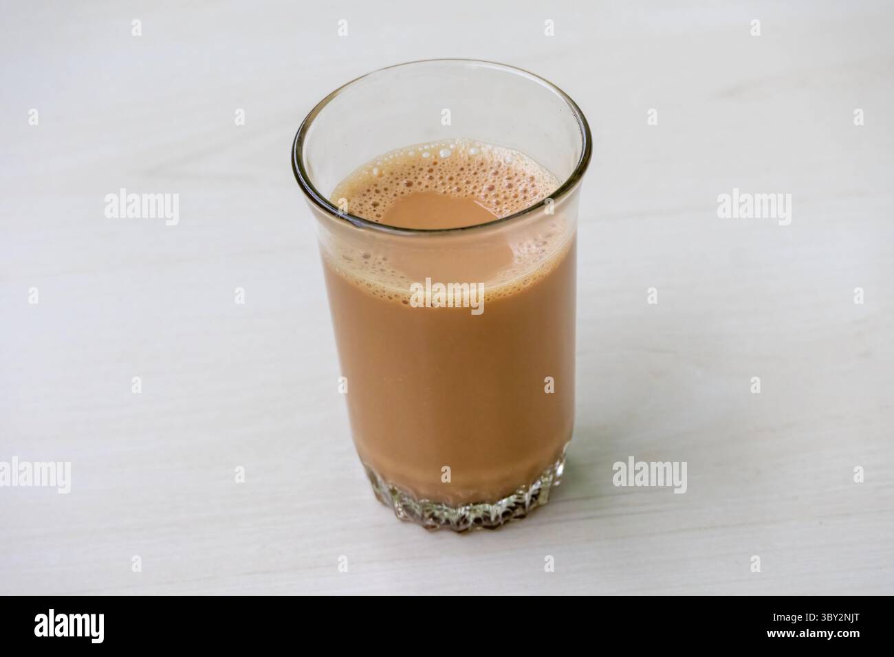 Delizioso tè al latte caldo con bollicine spugnose in una tazza di vetro trasparente su un tavolo di legno chiaro, perfetto per una piacevole fotografia di bevande e per concepire bevande. Foto Stock