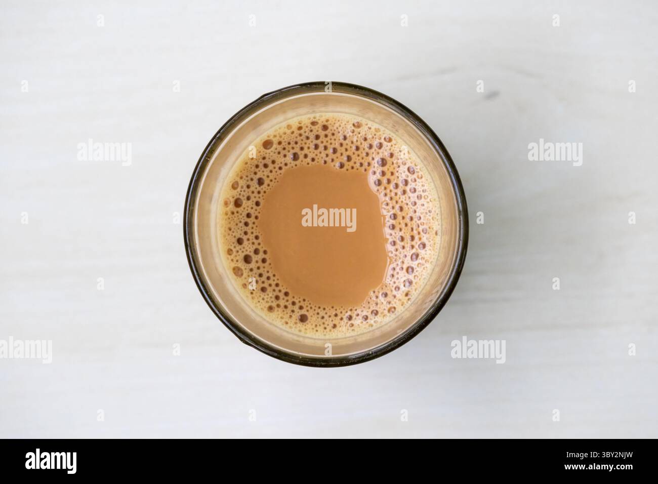 Tè al latte caldo e schiumoso con bollicine delicate, presentato in una tazza di vetro trasparente su una superficie di legno chiaro. Una vista dall'alto pulita e invitante per uno stile di vita Foto Stock