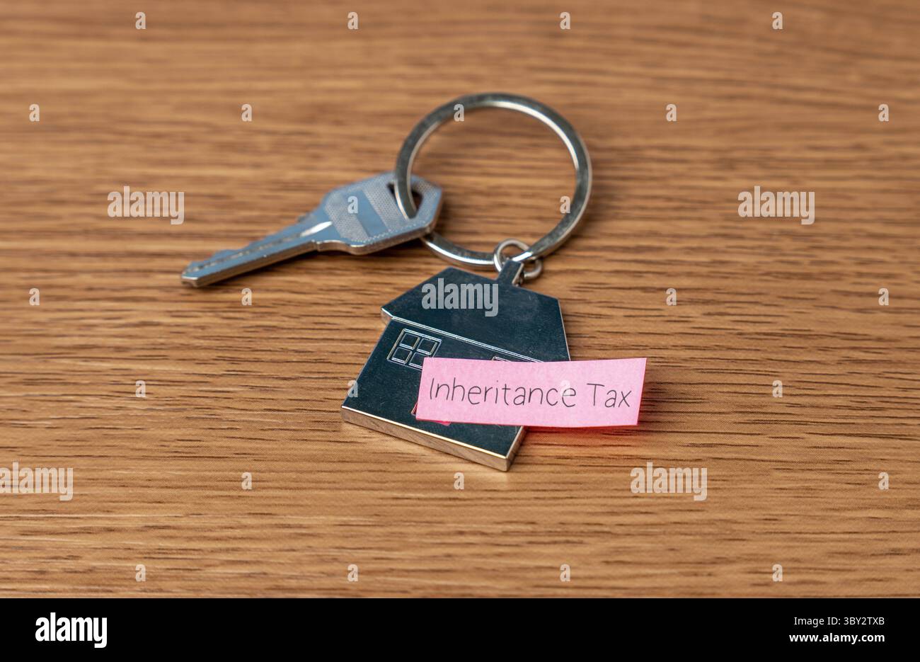 Un portachiavi a forma di casa con una chiave e una nota "imposta sull'eredità". Proprietà, eredità e concetto di tassazione associato. Foto Stock