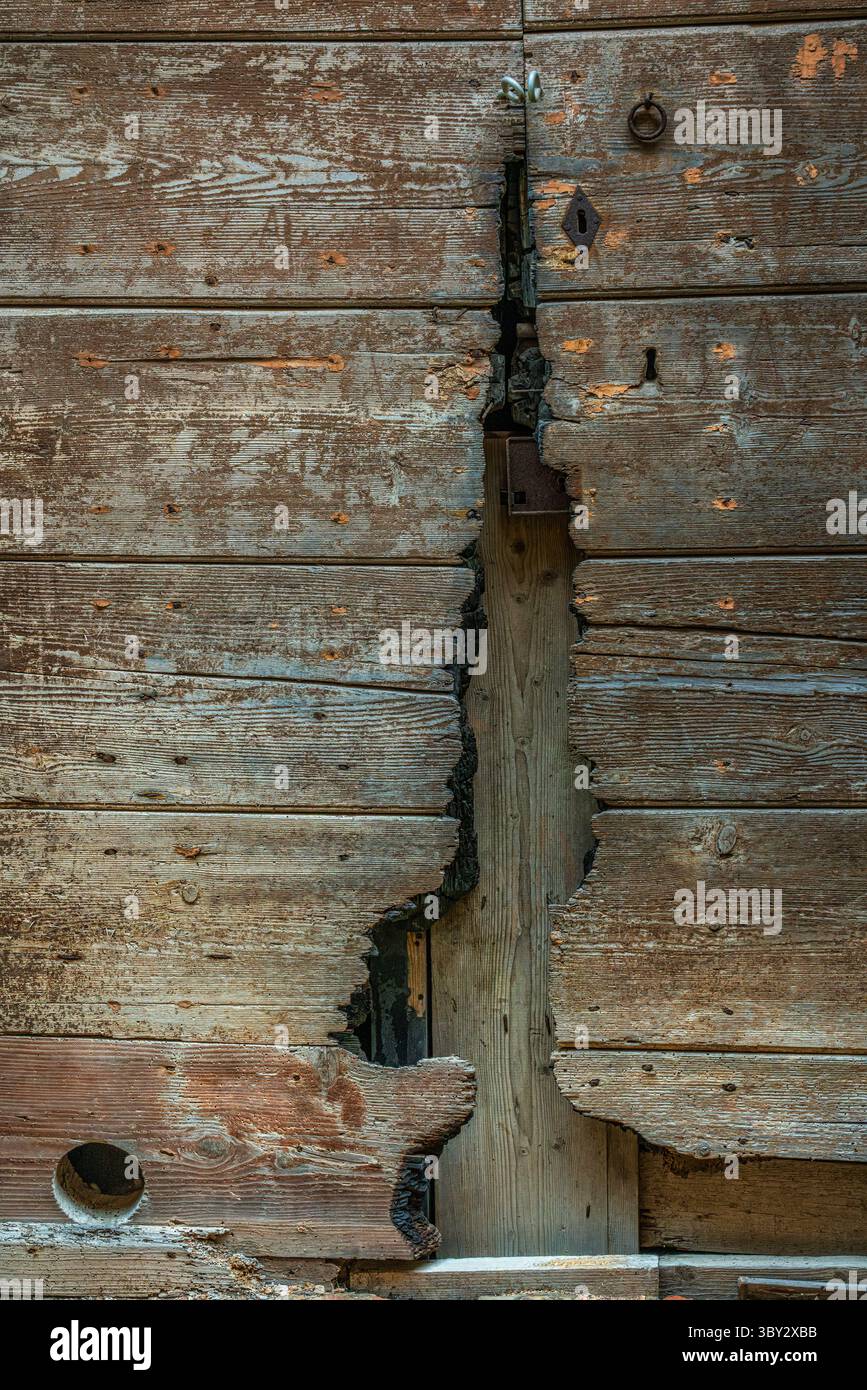 Una porta in legno incrinata con vernice staccabile e pannelli incrinati che rivelano il deterioramento dovuto a anni di esposizione. Ripatransone, Ascoli Piceno, Italia, Europa Foto Stock