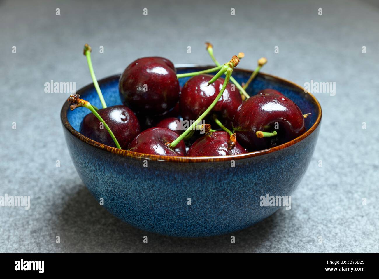 , Deutschland, 19.07.2025, Frisches Sommerobst: Eine blaue Keramikschale ist gefüllt mit saftig roten Kirschen. DAS natürliche Licht betont die glänz Foto Stock