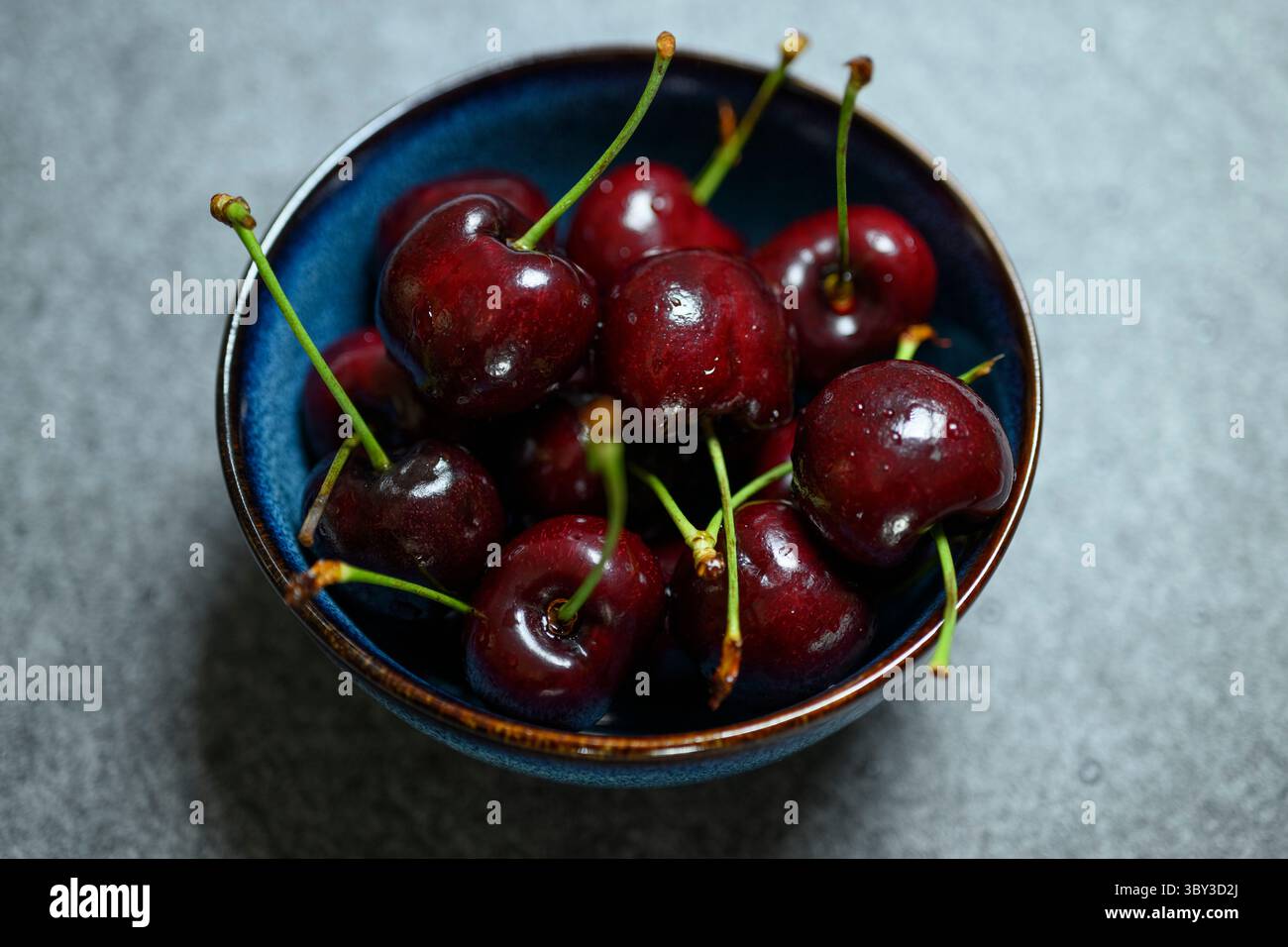 , Deutschland, 19.07.2025, Frisches Sommerobst: Eine blaue Keramikschale ist gefüllt mit saftig roten Kirschen. DAS natürliche Licht betont die glänz Foto Stock