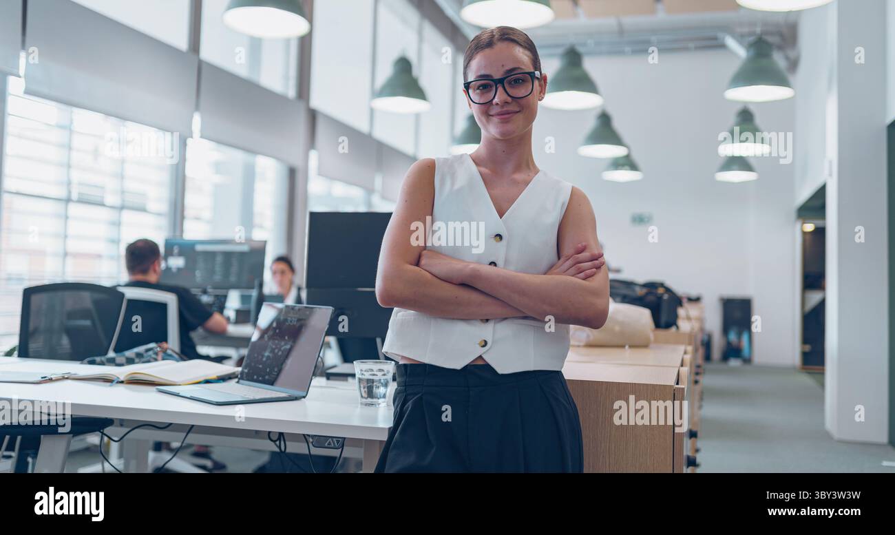 Una donna d'affari sicura di sé vive in un ambiente ufficio dinamico e moderno pieno di innovazione Foto Stock
