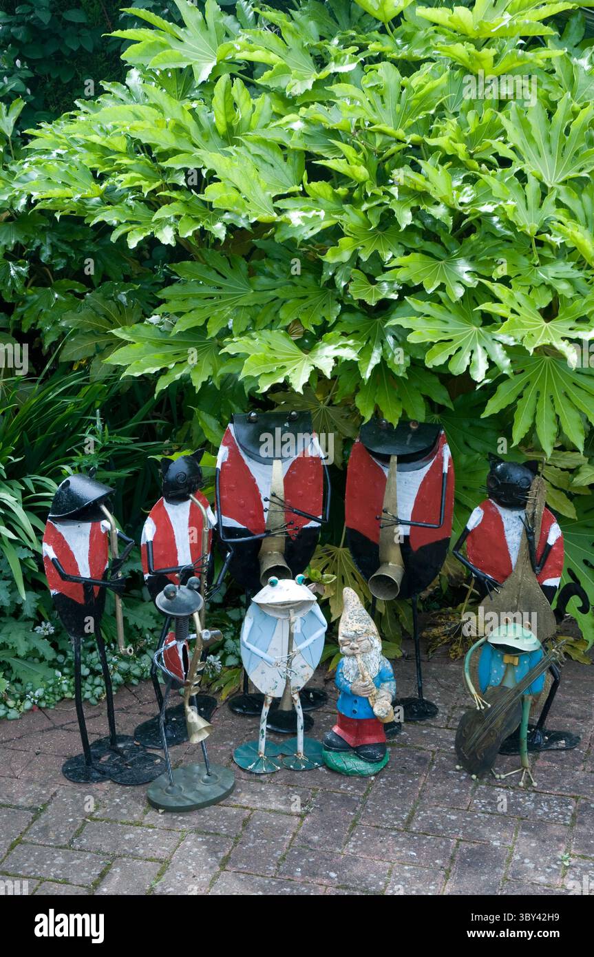 Figure in metallo stravaganti con abiti colorati si stagliano nel verde in un giardino, creando una mostra artistica di creatività. Foto Stock
