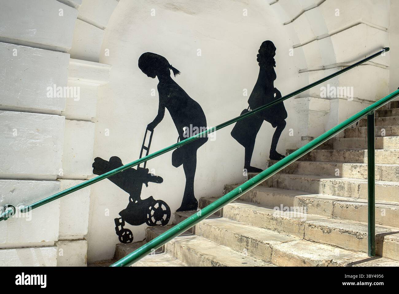 Bormla, Malta - 07.17.2025: Un dipinto murale vicino a una scala su una strada della città: Sagome di donne che camminano su per i gradini. Foto Stock Bormla, Malta - 07.17.2025: Un dipinto murale vicino a una scala su una strada della città: Sagome di donne che camminano su per i gradini. Foto Stock