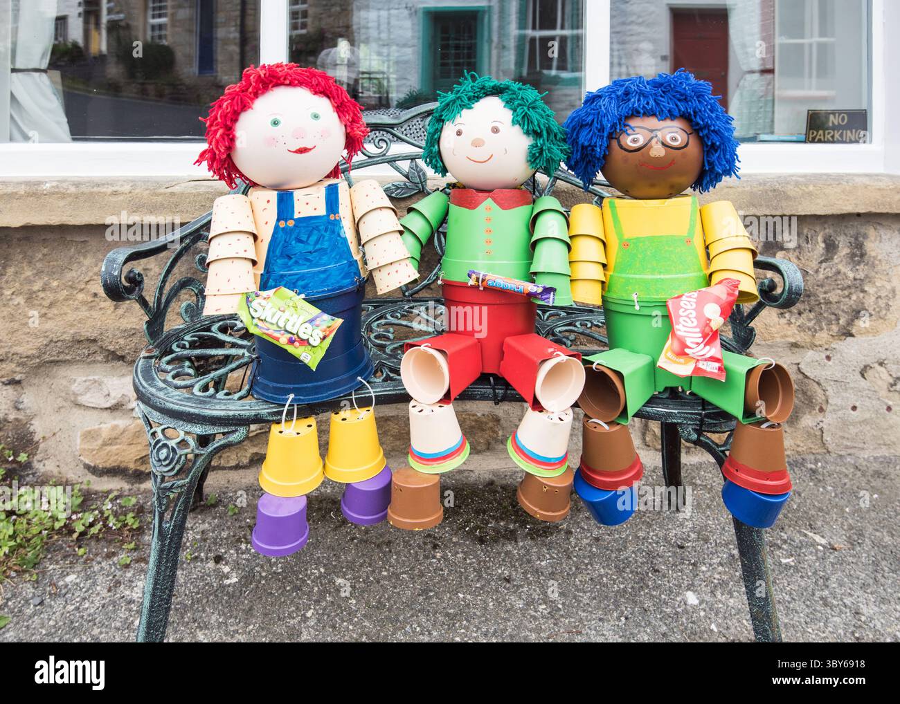 Stabilisci Flowerpot Festival 2025 con tre simpatici personaggi seduti su una panchina da giardino. Foto Stock