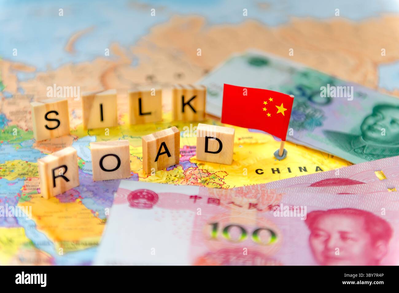 Un concetto di via della seta con piastrelle di lettere, banconote Yuan cinesi e bandiera nazionale su una mappa della Cina. Foto Stock