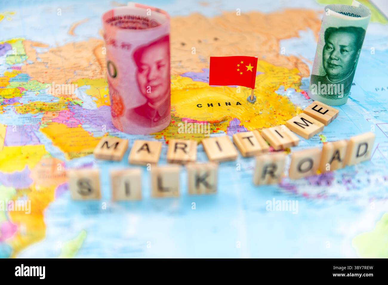 Un concetto di via della Seta marittima con piastrelle di lettere, rotoli di banconote cinesi in yuan e il nazionale su una mappa del mondo. Foto Stock