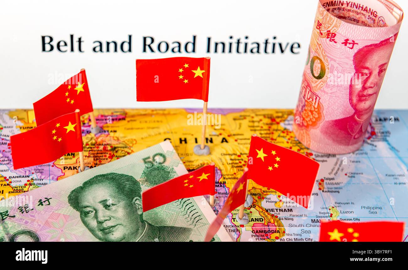 Un concetto di Belt and Road Initiative con bandiere nazionali cinesi e un mucchio di banconote Yuan su una mappa del mondo. Foto Stock