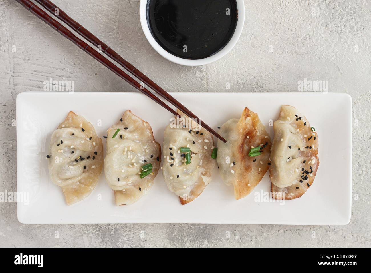 Gyoza gnocchi giapponesi, fritti, con salsa, cipolla verde e semi di sesamo, colore naturale, sfondo chiaro Foto Stock