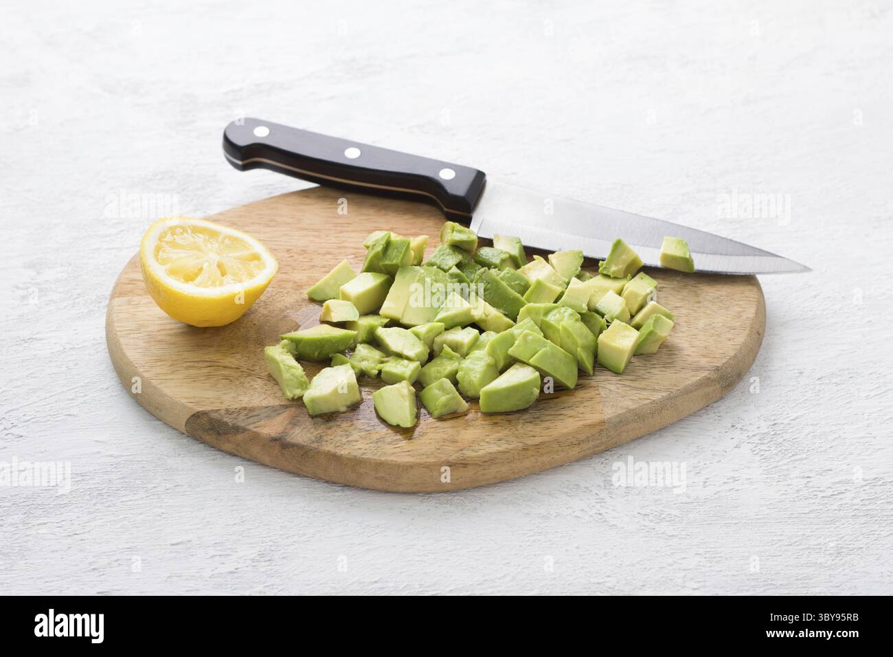 Cibo, tavola di legno con avocado tagliata a fette per insalata e cosparsa di succo di limone, mezzo limone e un coltello su sfondo grigio chiaro. Cucinare delizie Foto Stock