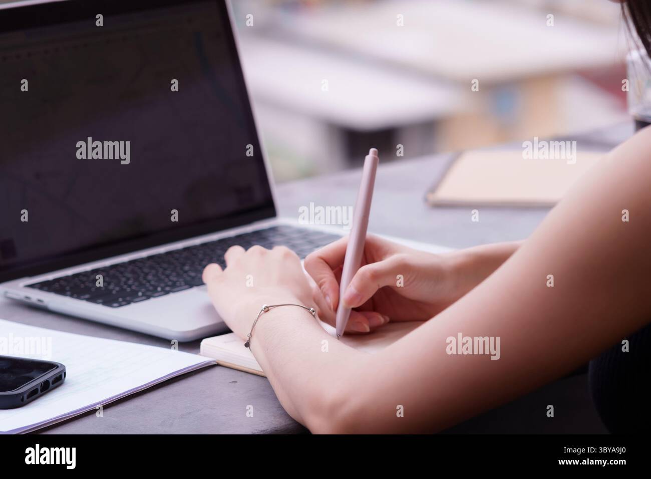 Mani professionali mirate che documentano meticolosamente le idee su un notebook vicino a un notebook, mostrando la moderna flessibilità del lavoro remoto e la connettività intelligente Foto Stock