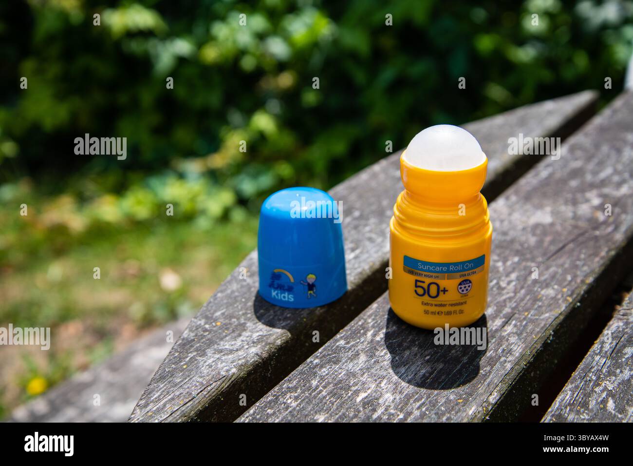 Protezione solare roll-on fattore 50+ giallo con coperchio blu aperto, che rivela la sfera a rulli. Posizionato su un tavolo da giardino in legno alla luce del sole, che mette in risalto Sun sa Foto Stock