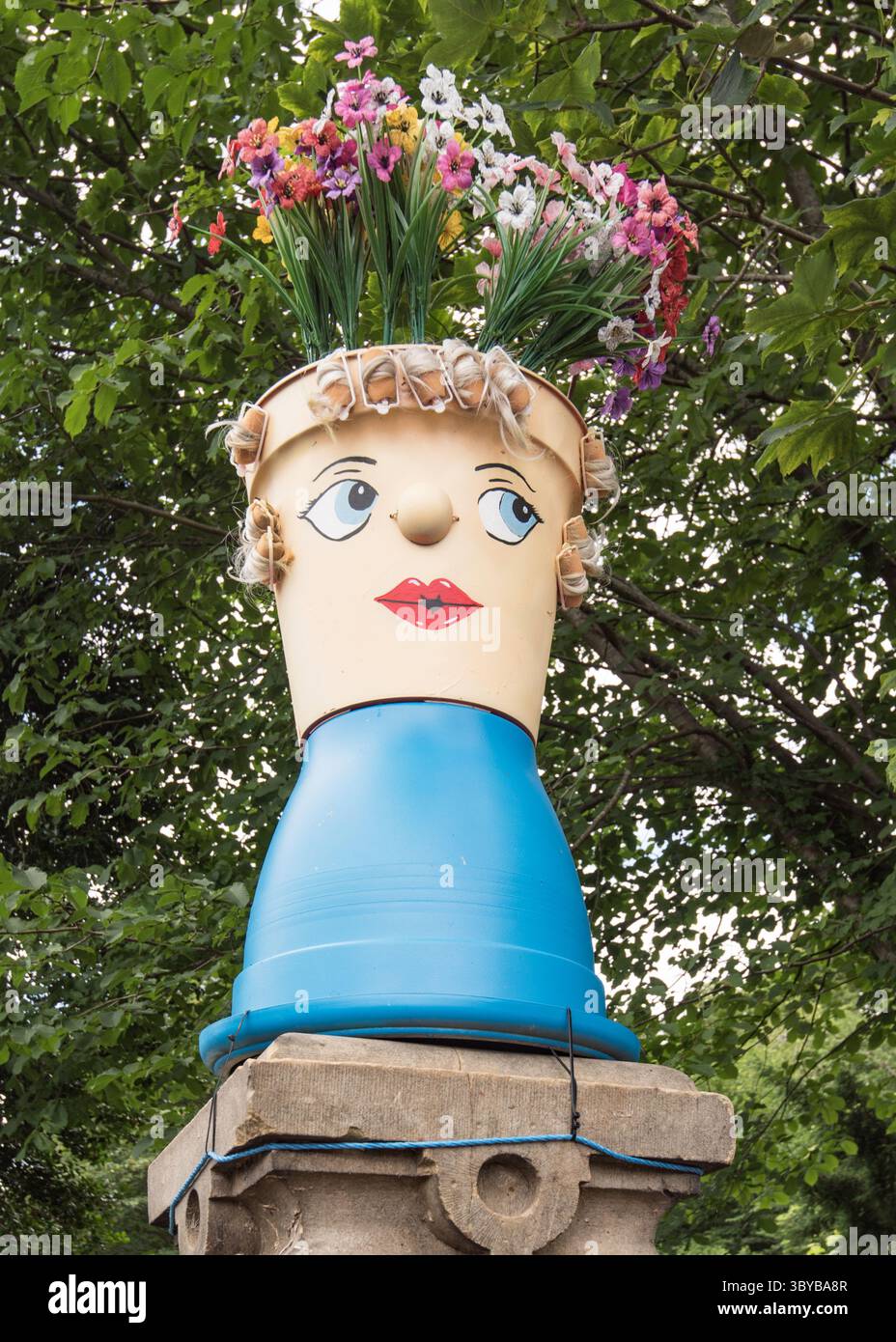Stabilisci il Flowerpot Festival 2025 con la crescita di fiori che sporge da un vaso di fiori che ha un volto dipinto su di esso. Foto Stock