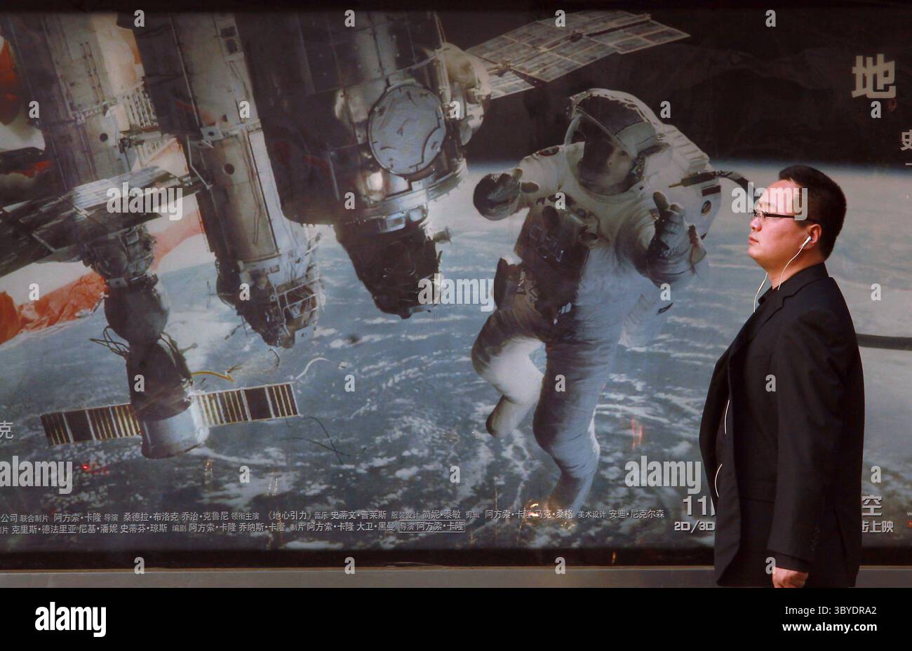 24 novembre 2013, PECHINO, CINA: Un uomo cinese aspetta un autobus di fronte a una pubblicità sul marciapiede per un film sugli astronauti americani e la stazione spaziale internazionale di Pechino il 24 novembre 2013. La Cina avrà l'opportunità, nel prossimo decennio, di superare gli Stati Uniti nei programmi spaziali, costringendo il governo degli Stati Uniti ad aumentare i finanziamenti della NASA per mantenere la sua posizione di leadership, entrare in partnership con i cinesi o rischiare di rimanere indietro, dicono gli esperti di politica spaziale. (Immagine di credito: © Stephen Shaver/ZUMA Press Wire) Foto Stock