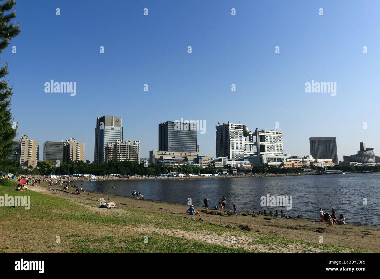 Vita quotidiana in Giappone persone che si rilassano sulla spiaggia di sabbia artificiale di Odaiba Seaside Park, con una vista panoramica del paesaggio urbano di Odaiba Foto Stock
