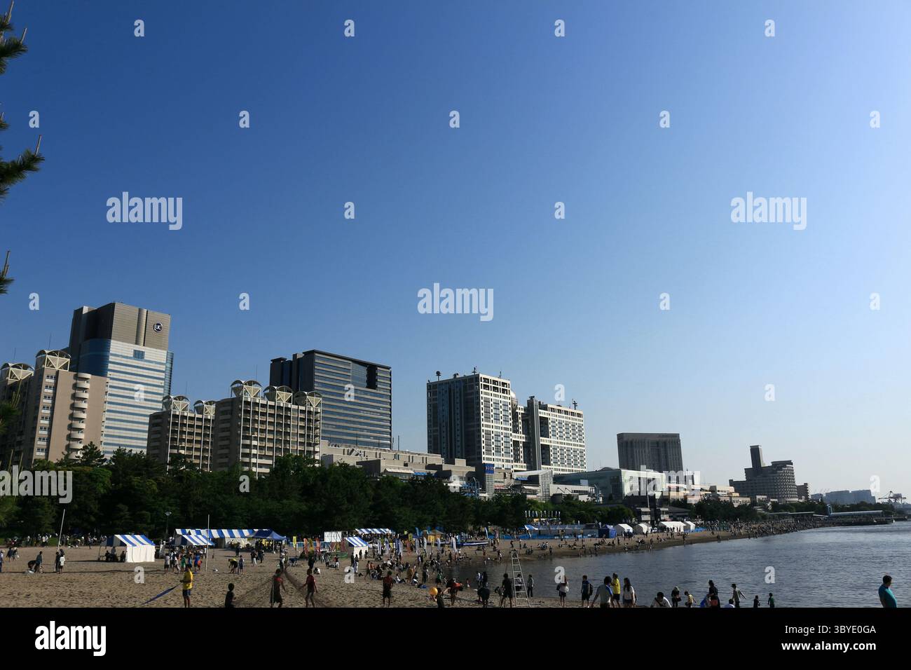 Vita quotidiana in Giappone persone che si godono la vita da spiaggia sulla spiaggia di sabbia artificiale di Odaiba Seaside Park, con una vista panoramica del paesaggio urbano di Odaiba Foto Stock