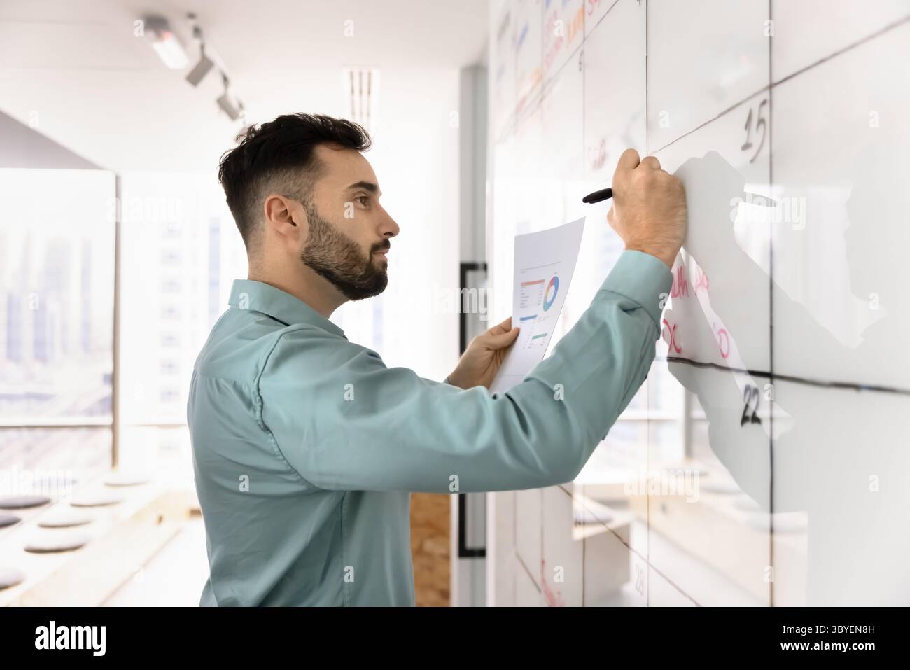 Uomo serio che tiene in mano documenti con grafici e scritte sulla lavagna Foto Stock