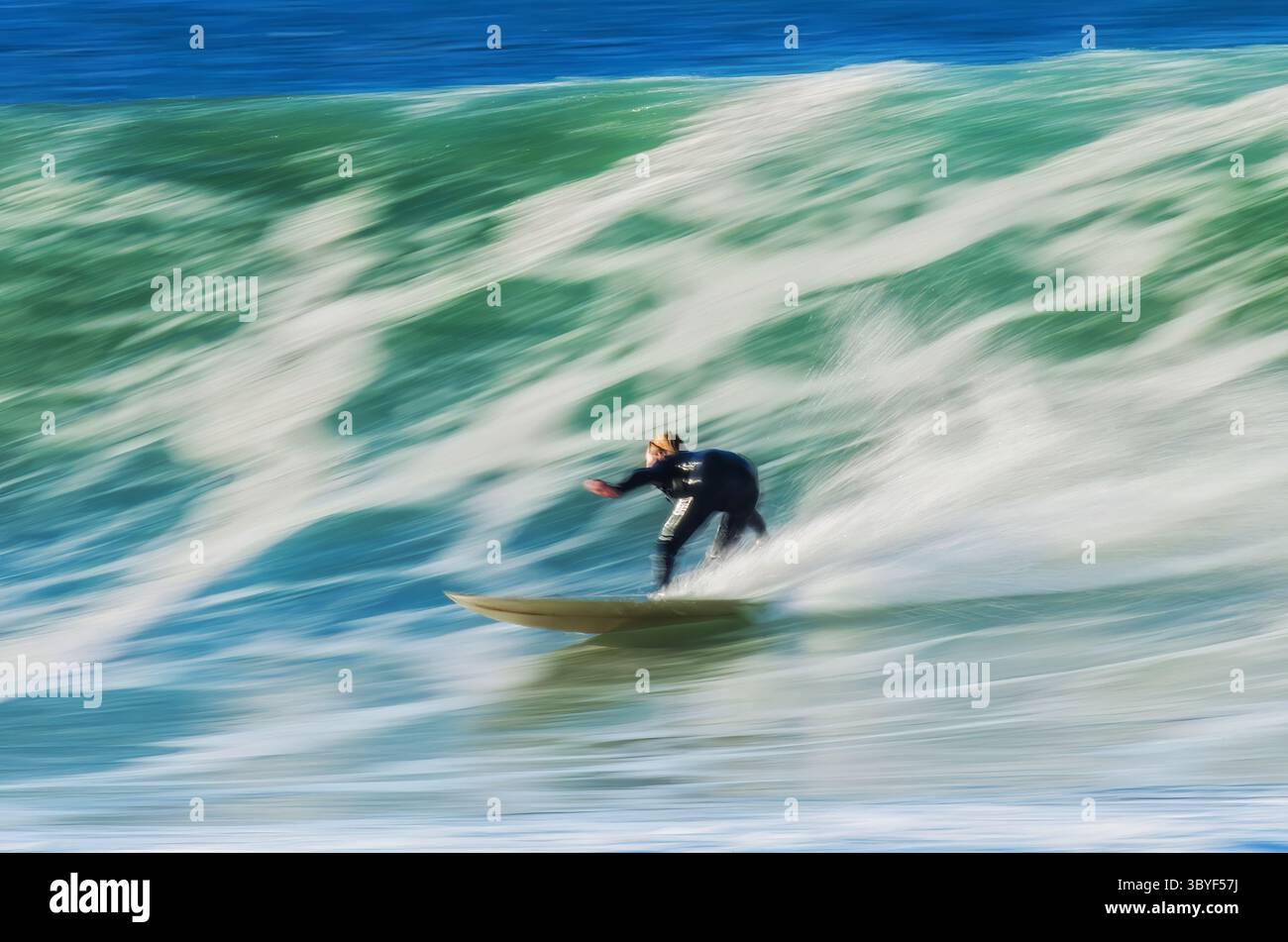 Un surfista scivola senza sforzo lungo un'onda torreggiante, catturando un momento di abilità e movimento Foto Stock