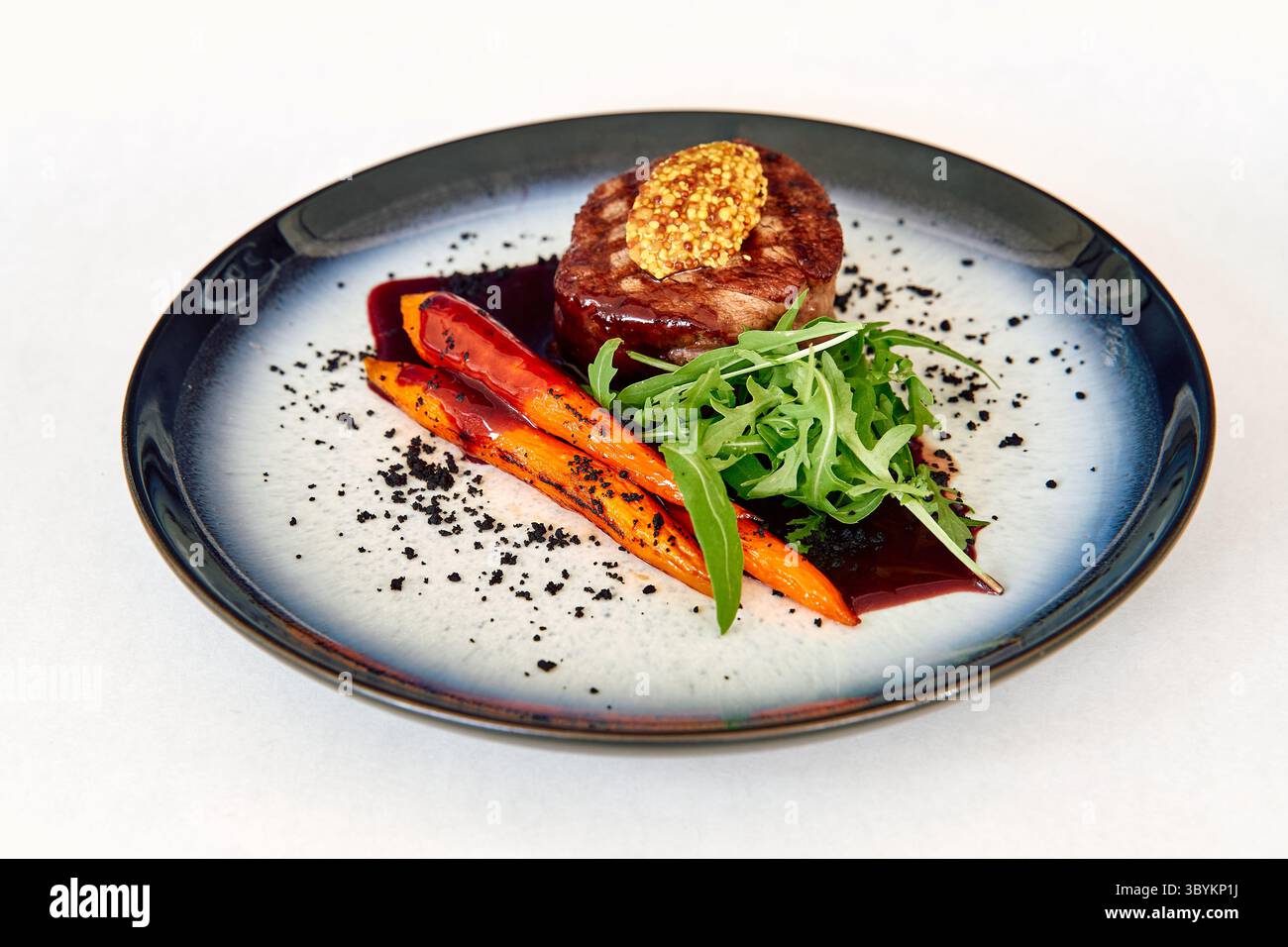 Saporito medaglione di manzo condito con senape, accompagnato da carote grigliate, verdure fresche e un crumble di oliva nero, per un cumino elegantemente presentato Foto Stock