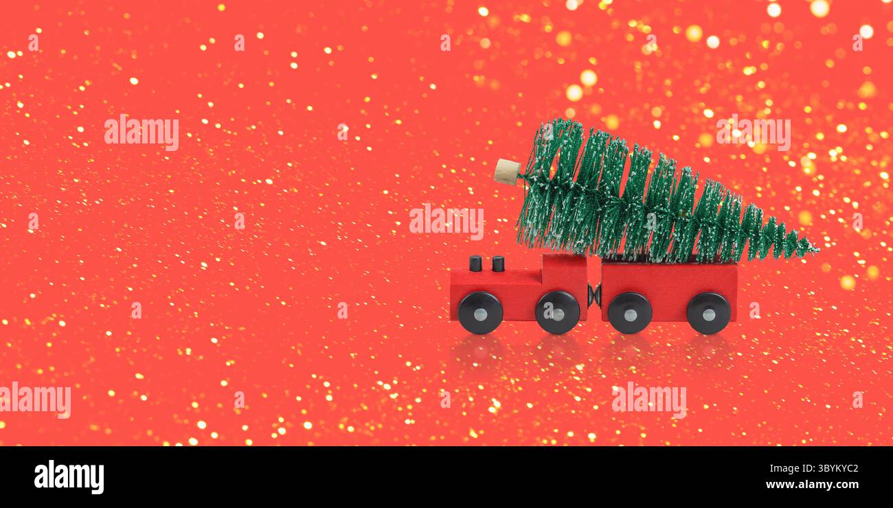 Composizione dell'albero di Natale verde e del treno a vapore rosso che trasporta l'albero di Natale su sfondo rosso con luci dorate per le feste. Concetto di Natale, ho Foto Stock