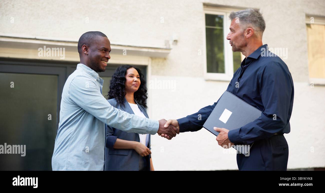Broker immobiliare sorridente che stringe la mano a una giovane coppia felice Foto Stock