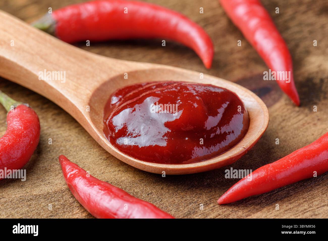 Cucchiaio di legno di pasta di peperoncino piccante tra peperoncini freschi Foto Stock