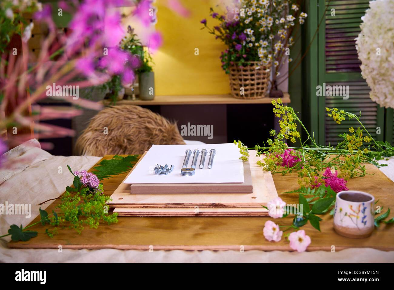 Kit per la stiratura dei fiori circondato da freschi fiori estivi. Progetto botanico fai da te in un ambiente accogliente con bulloni, tavole di legno e fogli di carta bianca Foto Stock