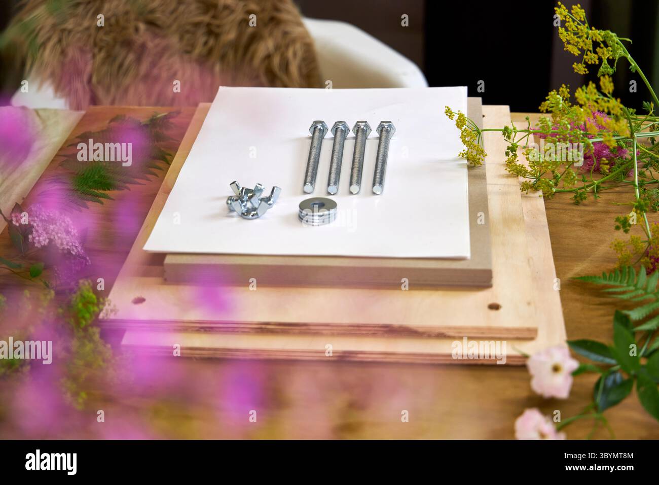 Kit per la stiratura dei fiori circondato da freschi fiori estivi. Progetto botanico fai da te in un ambiente accogliente con bulloni, tavole di legno e fogli di carta bianca Foto Stock