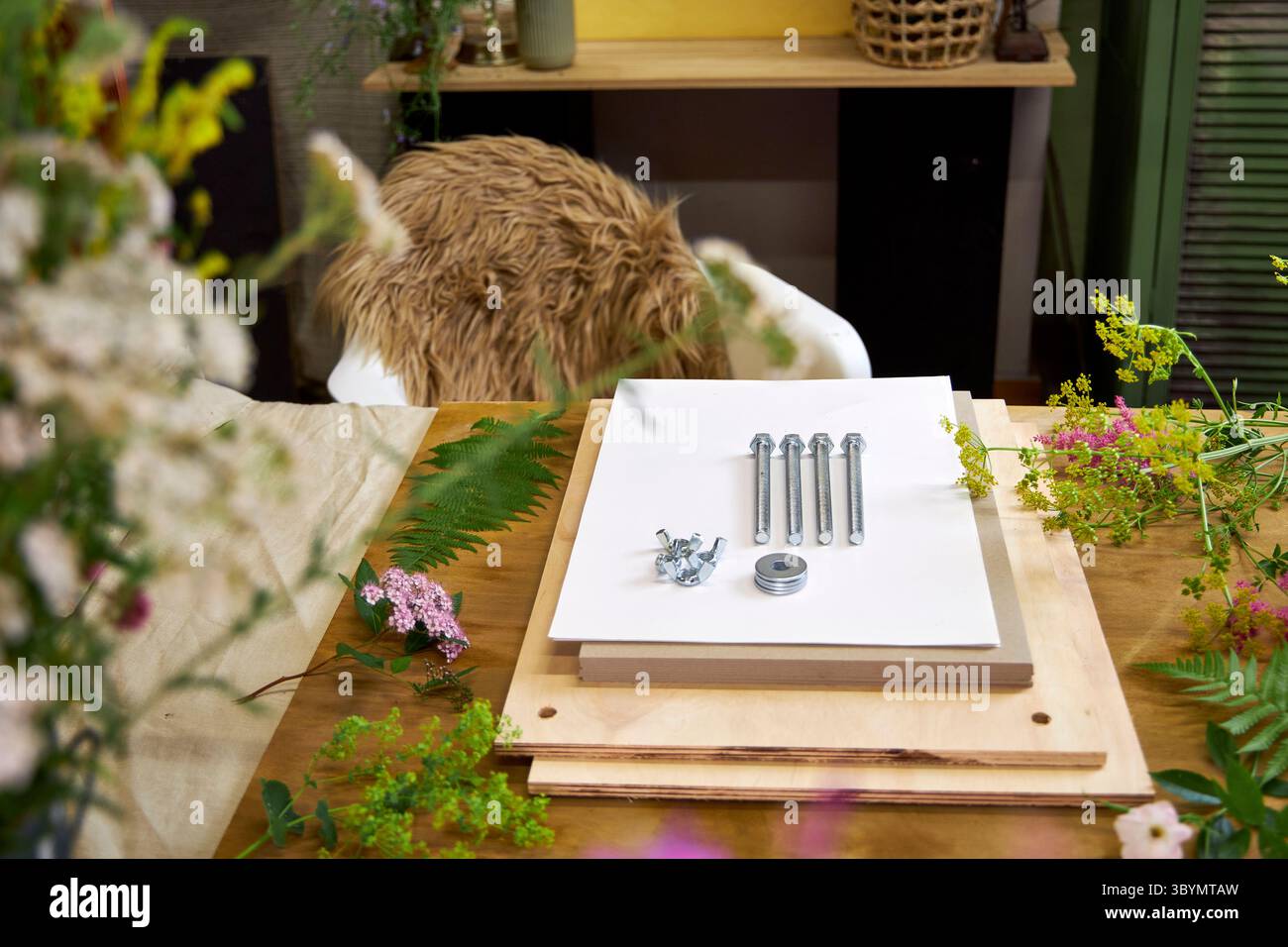 Kit per la stiratura dei fiori circondato da freschi fiori estivi. Progetto botanico fai da te in un ambiente accogliente con bulloni, tavole di legno e fogli di carta bianca Foto Stock