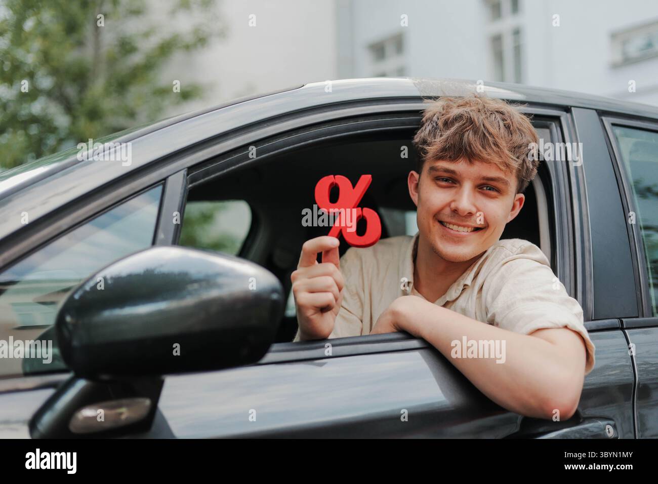 Giovane felice seduto all'interno della sua auto con il simbolo di percentuale rosso Foto Stock