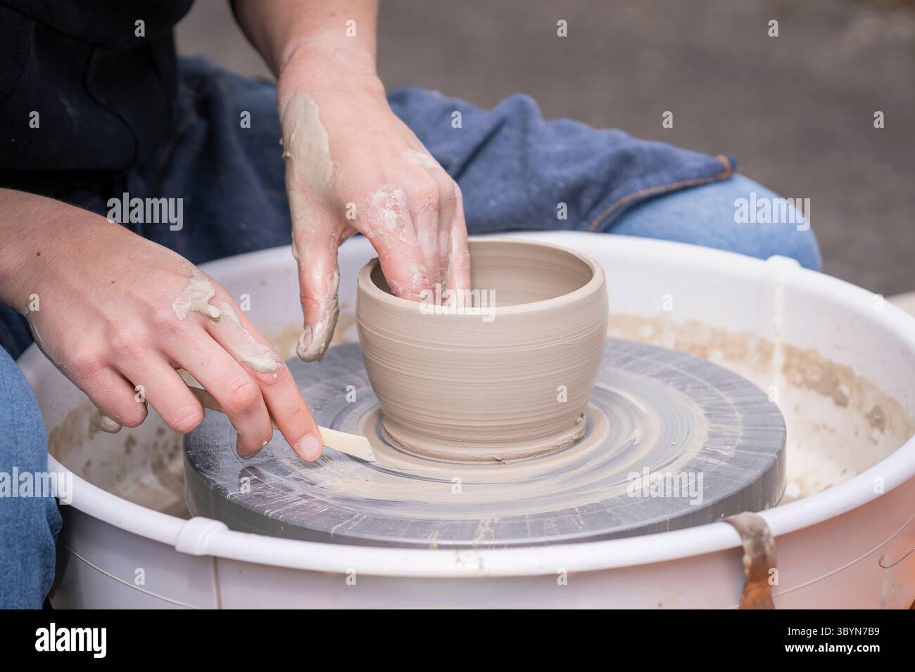 Primo piano di vaschette per preparare le mani. La donna ha cullato le mani intorno all'argilla bagnata su una ruota di vasai. Donna che produce ceramiche in un laboratorio di ceramica. Foto Stock