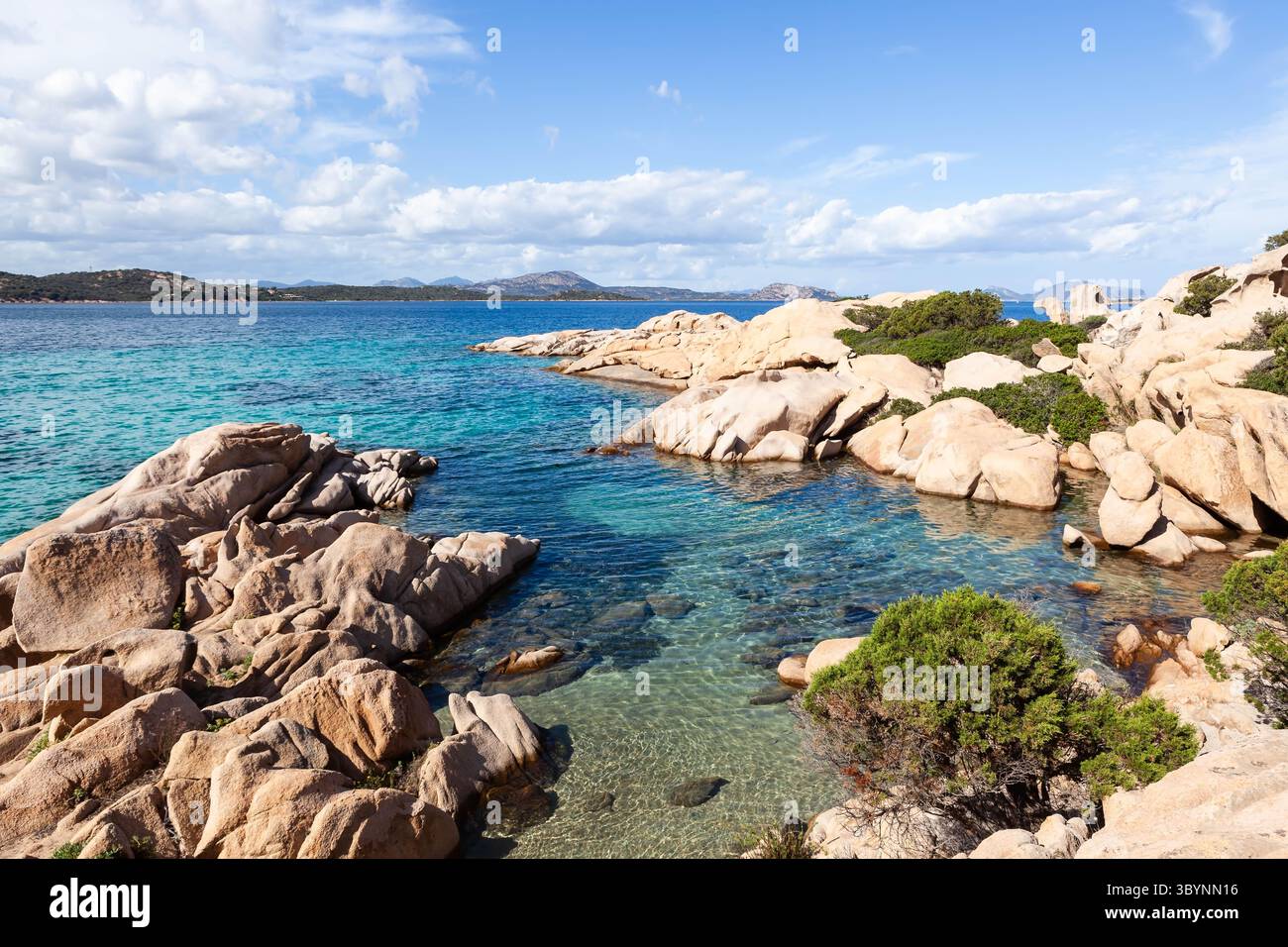 Una vista panoramica della costa rocciosa della Sardegna, Italia, con acque turchesi cristalline e un cielo blu con soffici nuvole. Foto Stock