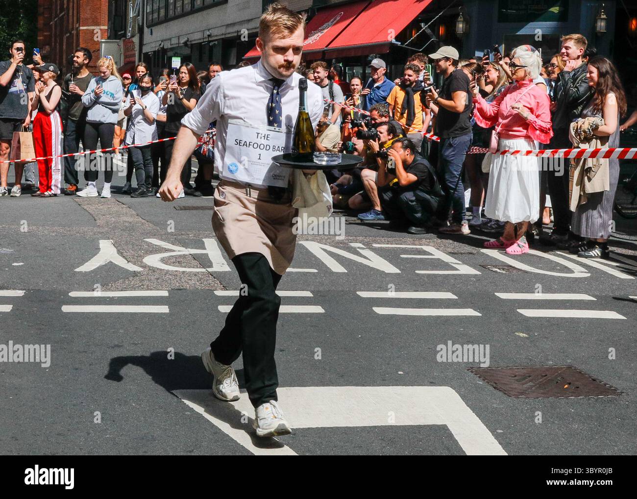 Londra, Regno Unito. 20 luglio 2025. Partecipanti lungo il percorso. L'annuale London Waiters' Race vede ancora una volta decine di camerieri, cameriere e personale di servizio correre a piedi per le strade di Soho, tenendo in mano un vassoio con champagne e bicchieri, che deve arrivare al traguardo intatto. La gara è una tradizione di Soho che attrae londinesi e visitatori. Crediti: Imageplotter/Alamy Live News Foto Stock