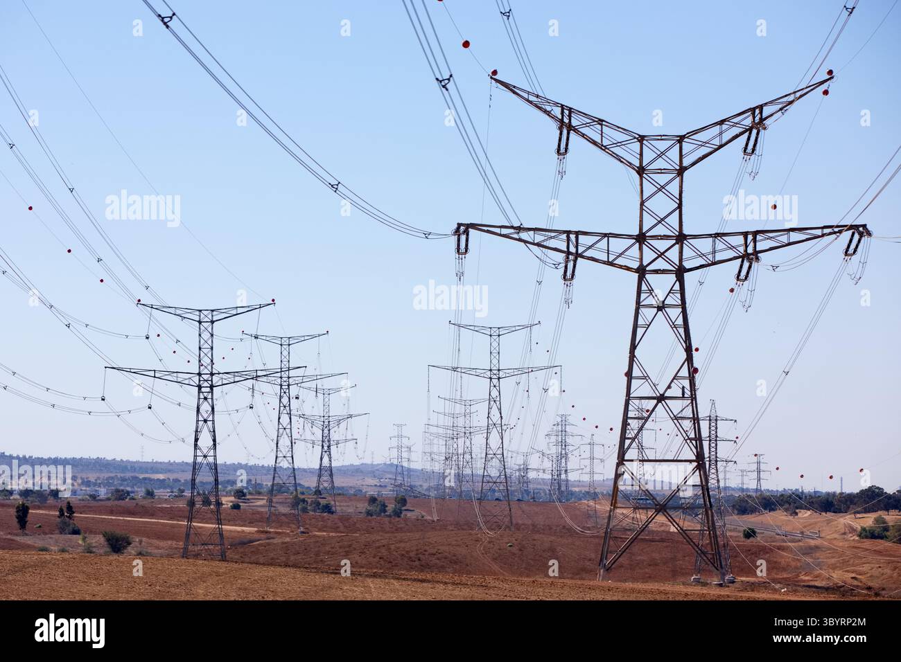 Le torri di trasmissione ad alta tensione marciano attraverso un paesaggio rurale illuminato dal sole sotto un cielo azzurro e limpido, le loro tralicci in acciaio evidenziano la scala industriale. Foto Stock Le torri di trasmissione ad alta tensione marciano attraverso un paesaggio rurale illuminato dal sole sotto un cielo azzurro e limpido, le loro tralicci in acciaio evidenziano la scala industriale. Foto Stock