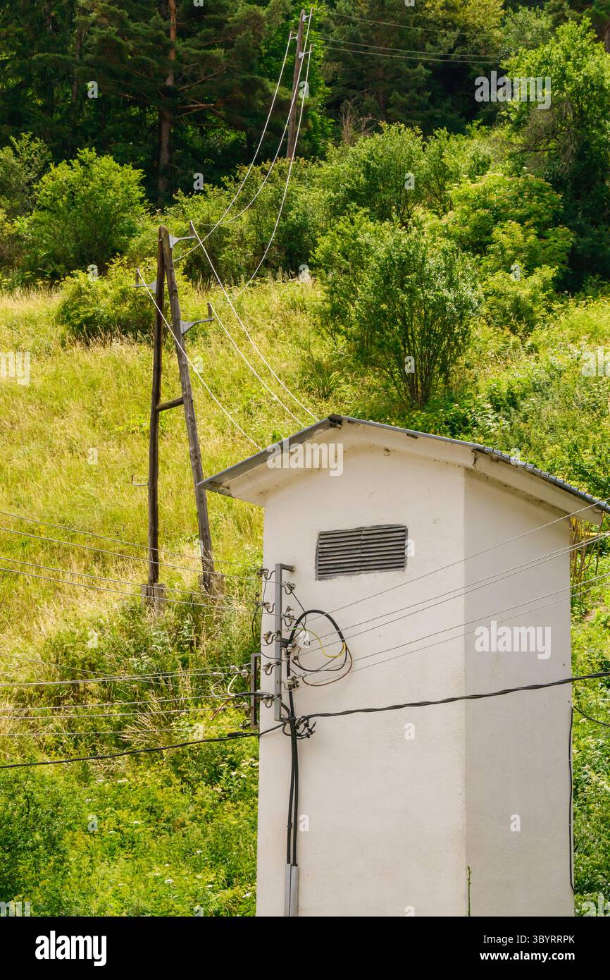 Una struttura di servizio sorge in un'area rurale circondata da lussureggianti colline verdi. Le linee elettriche passano in alto, collegando il sito remoto alla rete elettrica o Foto Stock