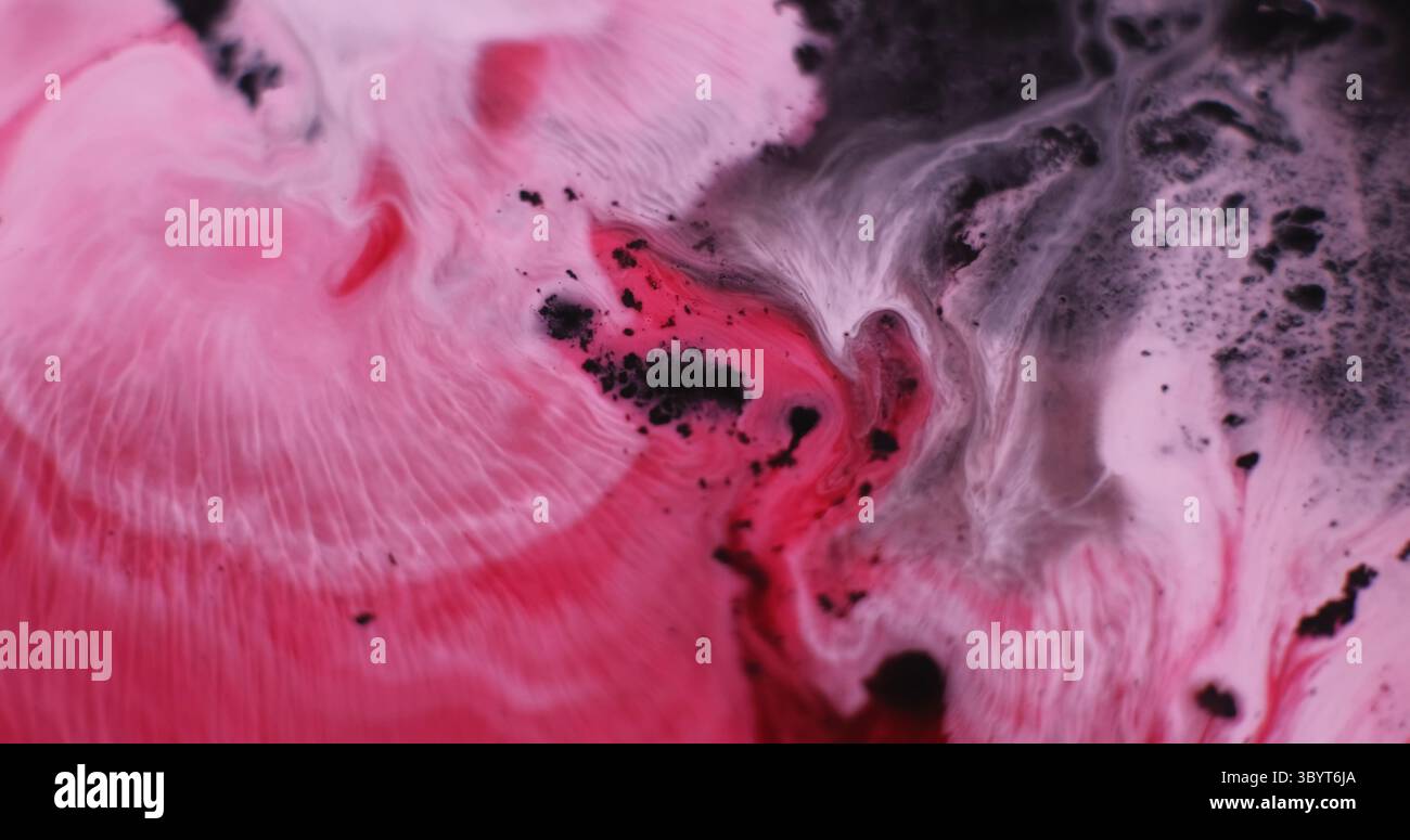 Spandimento della vernice. Mix di colori. Macchie ondulate fluide con emulsione d'acqua cremisi rosa defocalizzate su sfondo nero scuro con grafica astratta. Foto Stock