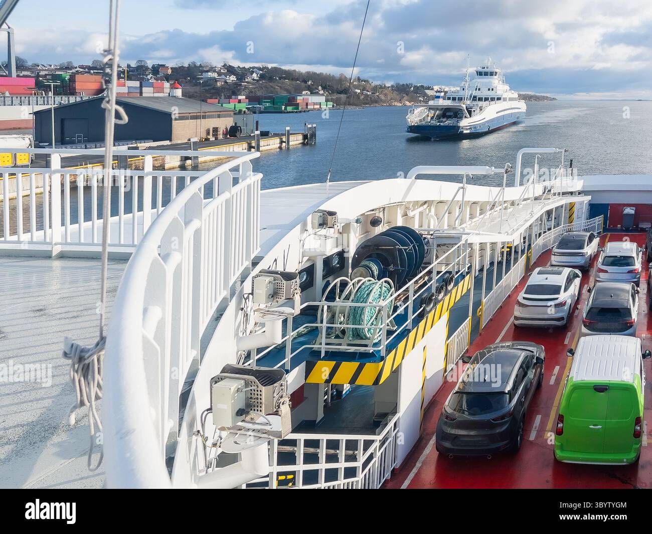 Il traghetto trasporta vari veicoli sul ponte, con una tranquilla vista sull'acqua e una terra lontana che crea un'atmosfera tranquilla Foto Stock
