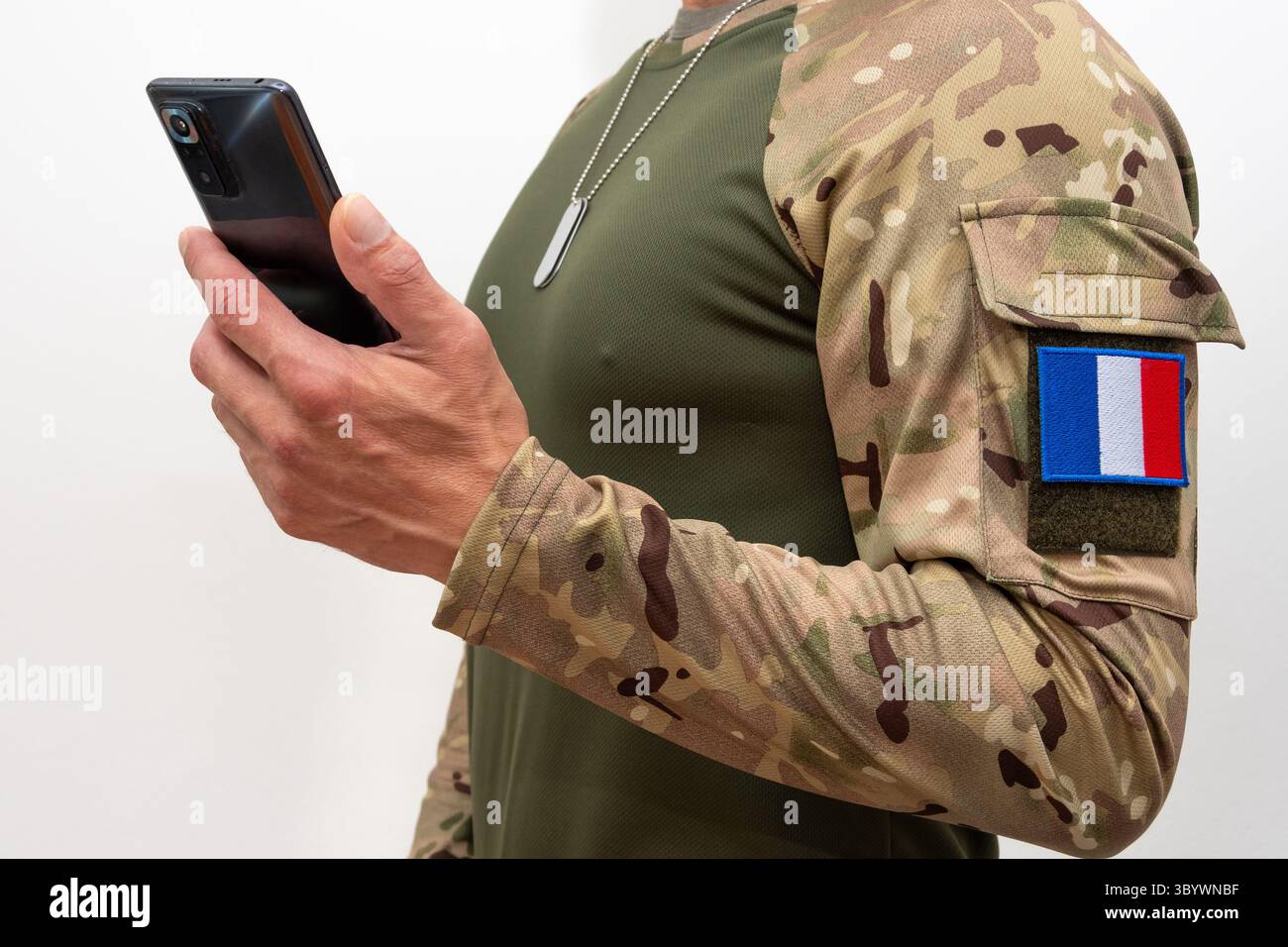 Un soldato in uniforme tattica con una patch bandiera francese e uno smartphone Foto Stock