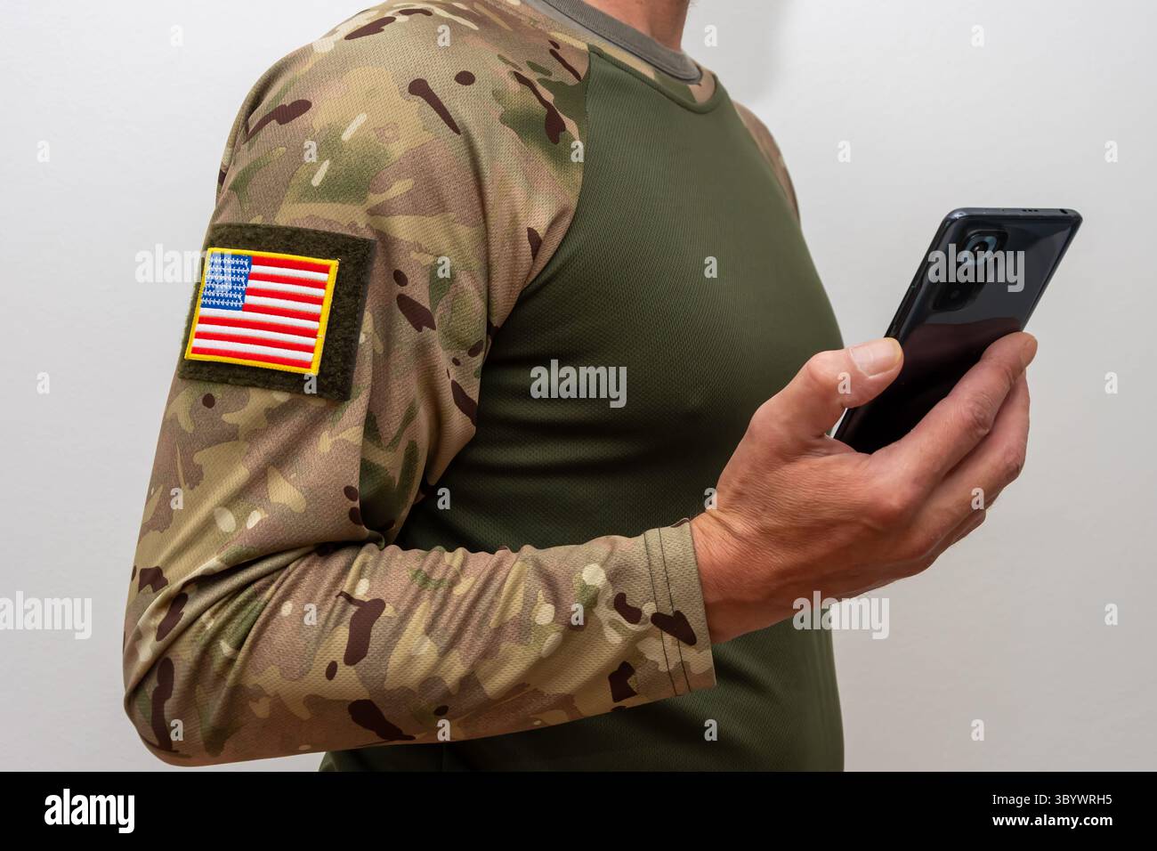 Un militare americano in mimetico con una bandiera statunitense sulla manica e uno smartphone in mano Foto Stock